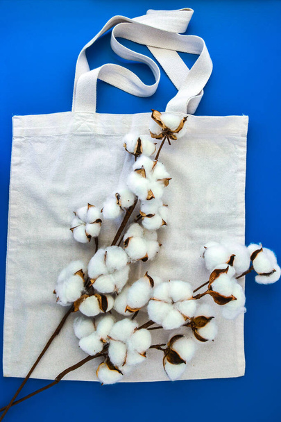 Elegantes bolsas ecológicas y flores de algodón sobre fondo azul, concepto de cero residuos. Compras ecológicas. Flores de algodón esponjoso y bolsas orgánicas, vista superior - Foto, Imagen
