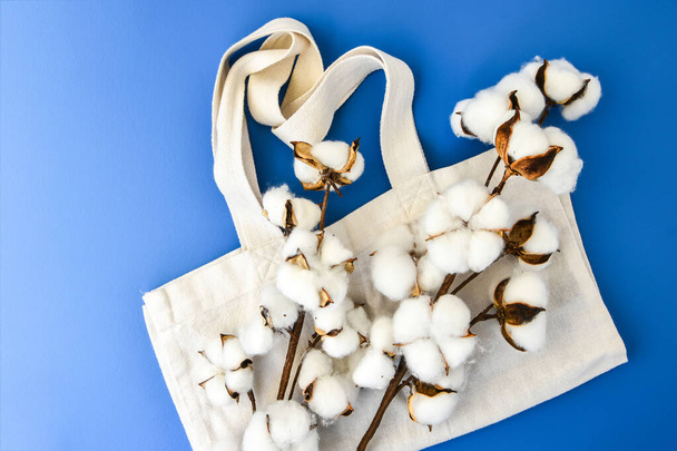 Elegantes bolsas ecológicas y flores de algodón sobre fondo azul, concepto de cero residuos. Compras ecológicas. Flores de algodón esponjoso y bolsas orgánicas, vista superior - Foto, imagen