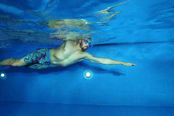 Fiatal férfi úszás a medencében lövés a víz alól, úszás koncepció - Fotó, kép