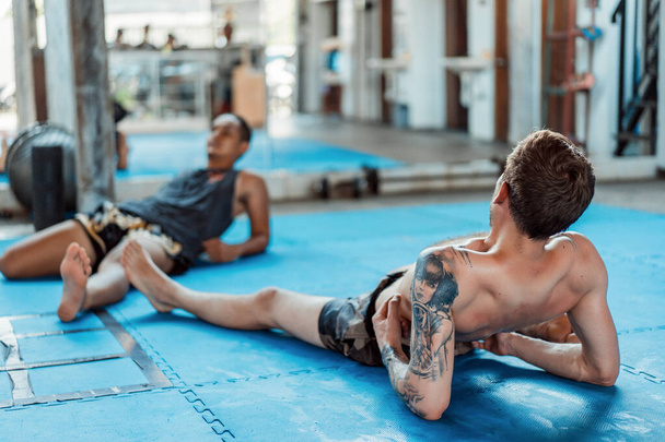 Training in the gym in the ring with a muay thai trainer. Tattooed caucasian man and Asian trainer. Muay thai training. - Foto, Imagem