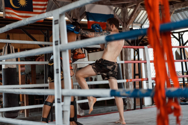 Ringde Muay Thai antrenörüyle antrenman yapmak. Dövmeli beyaz adam ve Asyalı antrenör. Muay thai eğitimi. - Fotoğraf, Görsel