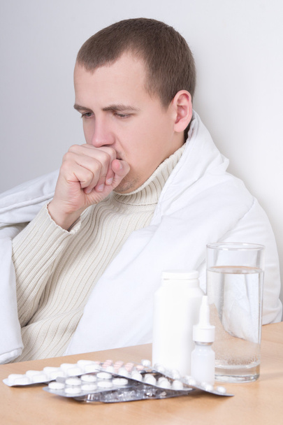 hombre joven de estornudo y pastillas en la mesa - Foto, imagen