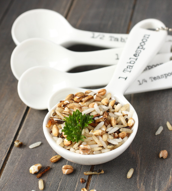 Uncooked multigrain rice in porcelain measuring spoons on wooden background - Foto, immagini
