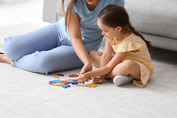 Little girl with autistic disorder and mother doing puzzle at home - Foto, imagen