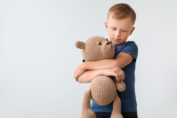 Trauriger kleiner Junge mit autistischer Störung und Spielzeug auf hellem Hintergrund - Foto, Bild