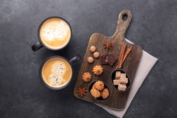 Black cups with coffee and various sweets on stone background. Coffee break. Top view. Copy space - Image - Φωτογραφία, εικόνα
