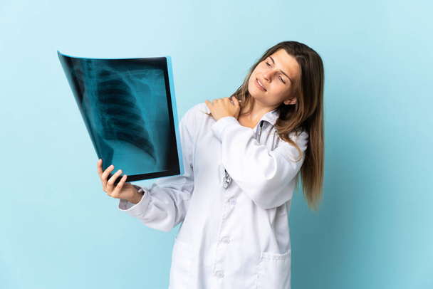 Joven doctora sosteniendo radiografía sobre fondo aislado sufriendo de dolor en el hombro por haber hecho un esfuerzo
 - Foto, Imagen