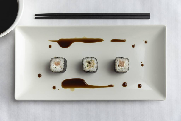 A top view of three sushi rolls on a plate with chopsticks on the table - Foto, imagen