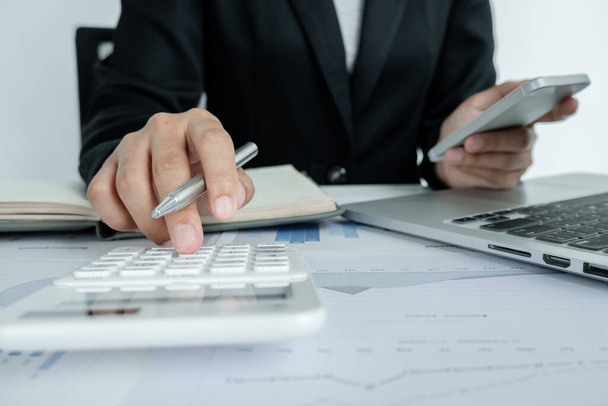 Руки предпринимательницы-мужчины используют калькулятор для анализа и расчета годового дохода и расходов в финансовом графике, который показывает результаты для обобщения балансов в целом в офисе. - Фото, изображение