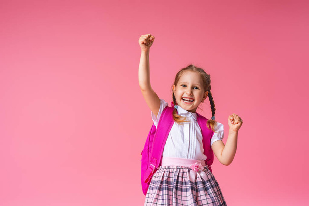 little schoolgirl screams loudly, happy to win on a pink background. A child in uniform with a backpack poses in the Studio. Back to school. School education is a lifestyle concept. - Photo, image