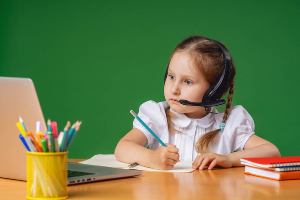 attentive little girl with headphones uses laptop to study on Internet, complete homework on distance learning during quarantine period. online learning. E-Education Distance Learning, Home Schooling. - Φωτογραφία, εικόνα