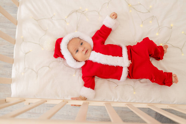 Christmas photo of a baby in a Santa suit lying in a crib at home, top view, happy new year. Christmas holiday concept - Valokuva, kuva