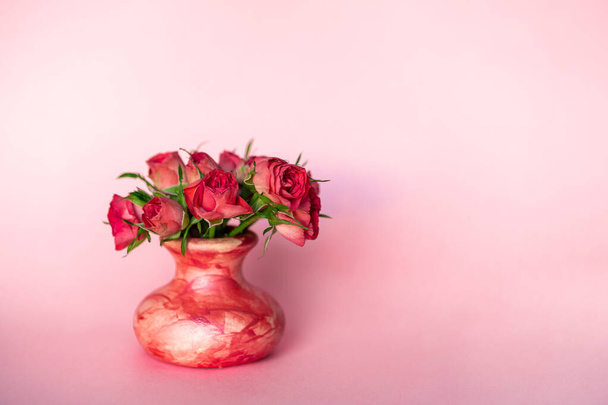 Πλευρική άποψη του μινιμαλιστικό προσφορά μικρό ροζ τριαντάφυλλο λουλούδι μπουκέτο σε μικρό κεραμικό βάζο σε παστέλ φόντο. Επίπεδη lay vintage ρετρό μοντέρνα χειροποίητα έργα τέχνης - Φωτογραφία, εικόνα