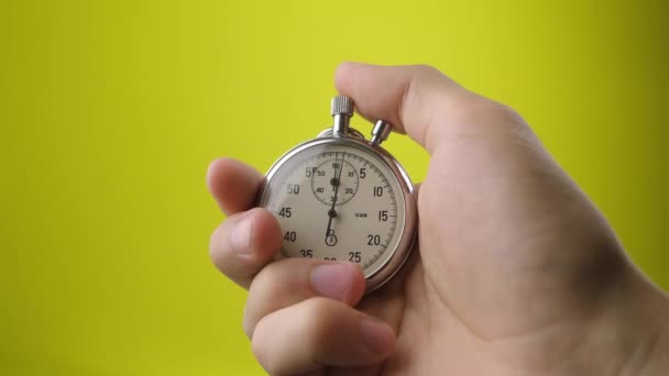 Male hand holding analogue stopwatch on yellow background. Time start with old chronometer man presses start button in the sport concept. Time management concept. - Footage, Video