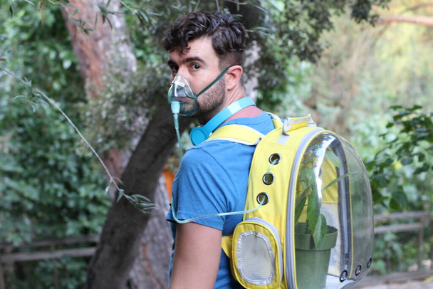 κοντινό πορτρέτο του όμορφου νεαρού άνδρα με φυτό σε σακίδιο πλάτης και μάσκα οξυγόνου στο πάρκο - Φωτογραφία, εικόνα