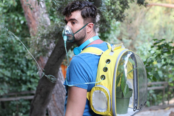 κοντινό πορτρέτο του όμορφου νεαρού άνδρα με φυτό σε σακίδιο πλάτης και μάσκα οξυγόνου στο πάρκο - Φωτογραφία, εικόνα