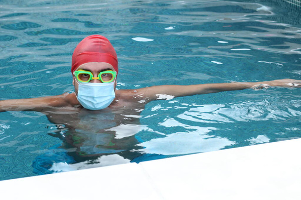 γκρο πλαν πορτρέτο του όμορφου νεαρού άνδρα με ιατρική προστατευτική μάσκα και γυαλιά κολύμβησης στην πισίνα κατά τη διάρκεια του εγκλεισμού του κορωναϊού - Φωτογραφία, εικόνα
