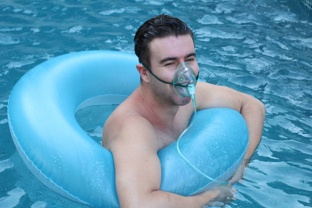 közeli kép egy jóképű fiatalemberről oxigénmaszkban felfújható gyűrűvel a medencében a koronavírus zárlat alatt - Fotó, kép