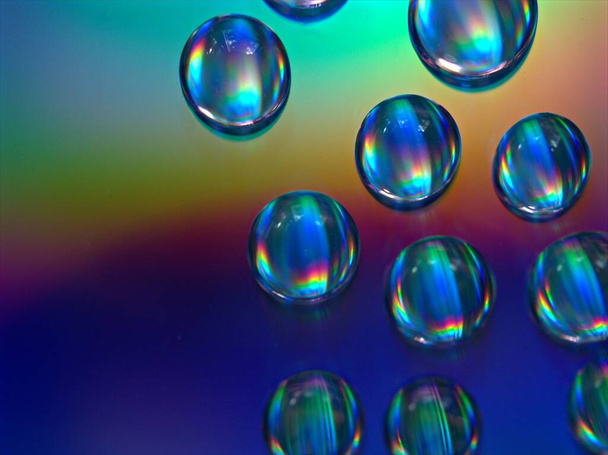 Close-up waterdruppels op kleurrijke en glanzende donkerblauwe achtergrond, macro afbeelding, kristallen druppels abstract, regenboog kleur - Foto, afbeelding