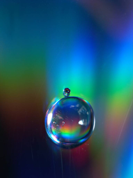 Close-up waterdruppels op kleurrijke en glanzende donkerblauwe achtergrond, macro afbeelding, kristallen druppels abstract, regenboog kleur - Foto, afbeelding