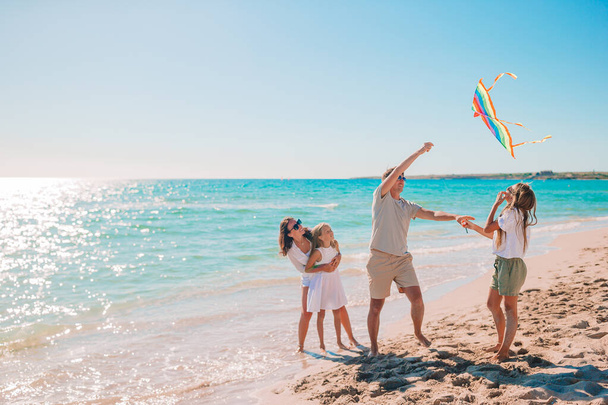 Счастливая молодая семья с двумя детьми с запуском воздушного змея на пляже - Фото, изображение