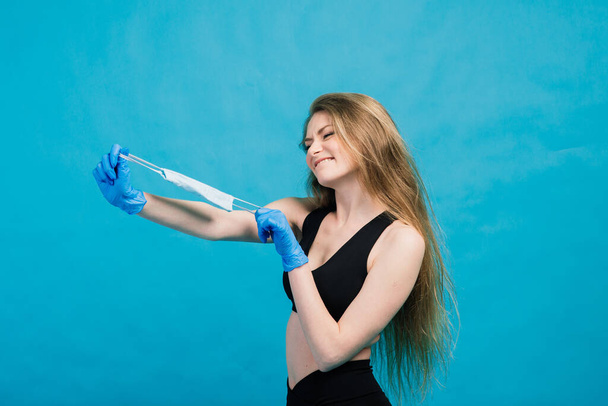 Fitness girl wearing medicine mask in fitness costume isolated on blue background. Training during quarantine, covid 19, corona virus. - Foto, afbeelding