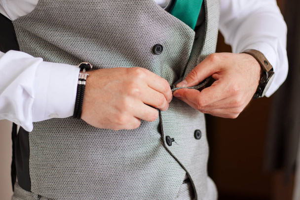 Großaufnahme von männlichen Händen, die Weste aus grauem Anzug zuknöpfen. Mann bereitet sich auf formelles Ereignis vor.  - Foto, Bild