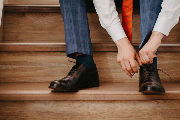 Επιχειρηματίας δένοντας τα παπούτσια, ενώ κάθεται σε ξύλινες σκάλες στο σπίτι, ετοιμάζεται για την εργασία.  - Φωτογραφία, εικόνα