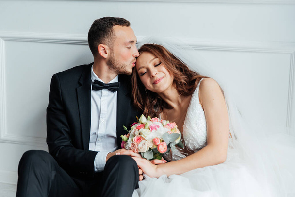 Das erste Treffen des Bräutigams im schwarzen Anzug und der Braut im weißen Hochzeitskleid mit Blumenstrauß im Inneren eines Fotostudios auf weißem und schwarzem Hintergrund - Foto, Bild