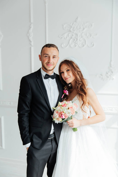Das erste Treffen des Bräutigams im schwarzen Anzug und der Braut im weißen Hochzeitskleid mit Blumenstrauß im Inneren eines Fotostudios auf weißem und schwarzem Hintergrund - Foto, Bild