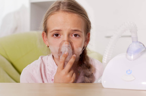 Young girl using a nebulizer inhaler device with mist shooting out of the mouthpiece - respiratory disease and allergy relieve concept - Фото, изображение