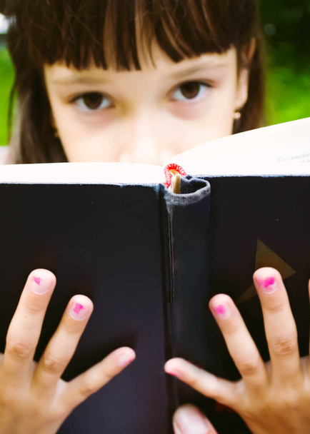 schöne und glückliche junge Studentin, die auf einer Bank mit Buch sitzt, ihre Hände auf einem Stapel Bücher, in die Kamera schaut und lächelt. Sommer oder Frühling grüne Park im Hintergrund. Weichzeichner-Foto - Foto, Bild
