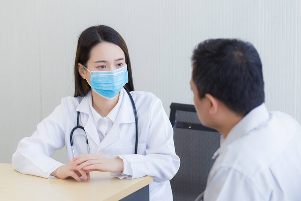 Концепция коронавирусной защиты. Врач-азиатка задаёт пациентке вопросы, постоянно надевая хирургическую маску. - Фото, изображение