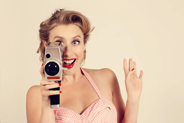 portret młodej atrakcyjnej blondynki sexy vintage pin-up kobieta filmowanie ze starym aparatem na izolowanym tle studio - Zdjęcie, obraz