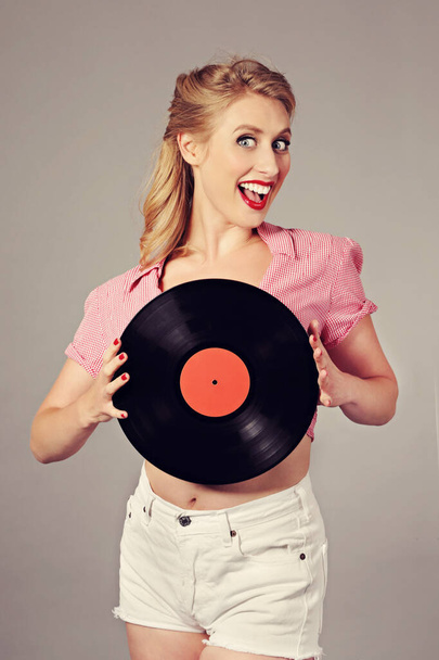 funny portrait of a young attractive blonde sexy vintage pin-up woman holding a vinyl record on isolated studio background - Fotografia, imagem