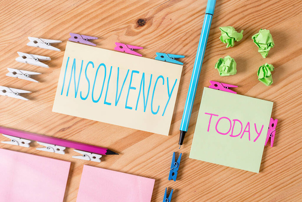 Handwriting text writing Insolvency. Concept meaning the state of being insolvent inability to pay one s is debts Colored clothespin papers empty reminder wooden floor background office. - Photo, Image
