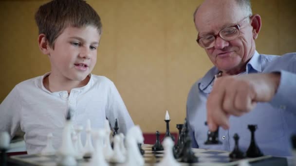 lapsen kehitys, iloinen isoisä, jolla on lasit näköä ja onnellinen pojanpoika hymyilevät ja pelaavat shakkia - Materiaali, video