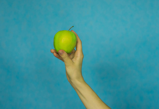 Die Hand einer Frau hält einen reifen Apfel auf blauem Hintergrund. Gesunde Ernährung.Vitamine. - Foto, Bild