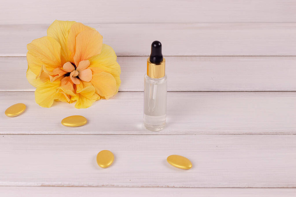 samenstelling van een gele bloem en serum in een glazen reageerbuis op een witte houten ondergrond. Kopieerruimte - Foto, afbeelding