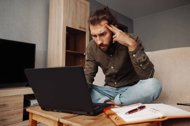 A pensive man works at a laptop at home, reflects on work. Online home education - Foto, Imagen