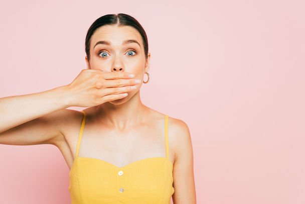 shocked brunette young woman covering mouth with hand isolated on pink - Fotografie, Obrázek
