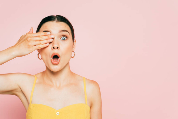 surprised brunette young woman covering eye isolated on pink - Photo, image