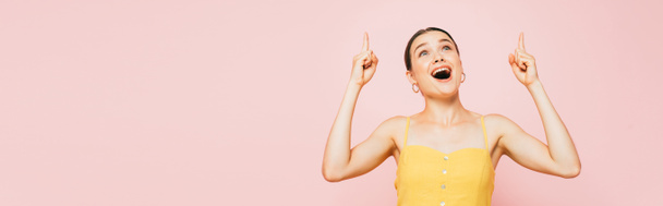 excited brunette young woman pointing with fingers up isolated on pink, panoramic shot - Photo, Image