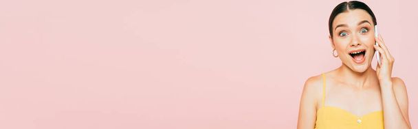 excité brunette jeune femme parler sur smartphone isolé sur rose, panoramique shot - Photo, image