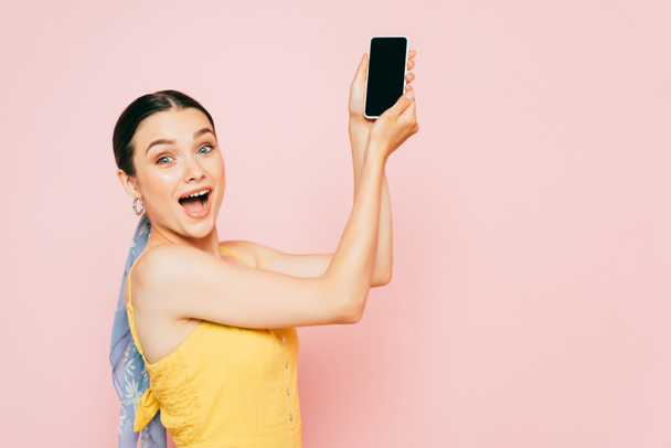 side view of brunette young woman holding smartphone isolated on pink - Fotó, kép