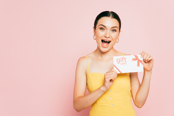 excited brunette young woman holding gift card isolated on pink - Fotoğraf, Görsel
