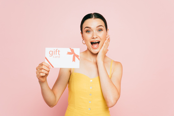 excited brunette young woman holding gift card isolated on pink - Photo, Image