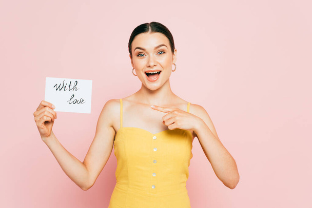 surprised brunette young woman pointing at with love card on pink - Photo, Image