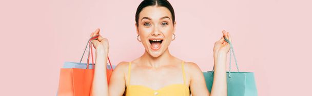 podekscytowany brunetka młoda kobieta z torby na zakupy odizolowane na różowy, panoramiczny strzał - Zdjęcie, obraz