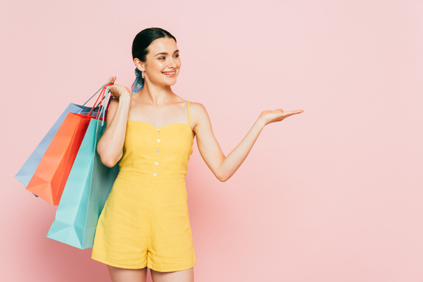 brunette young woman with shopping bags pointing with hand aside on pink - Fotografie, Obrázek